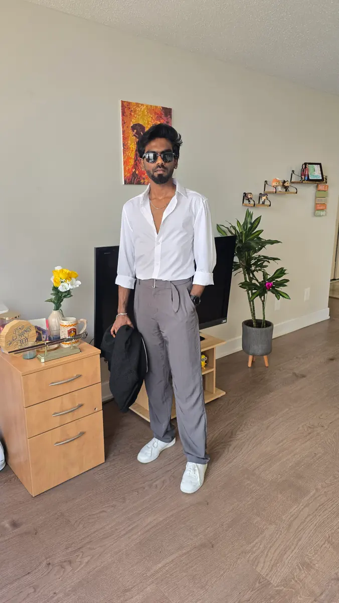 Vijay at home in an open white shirt and grey trousers, sunglasses on, a jacket draped over one arm