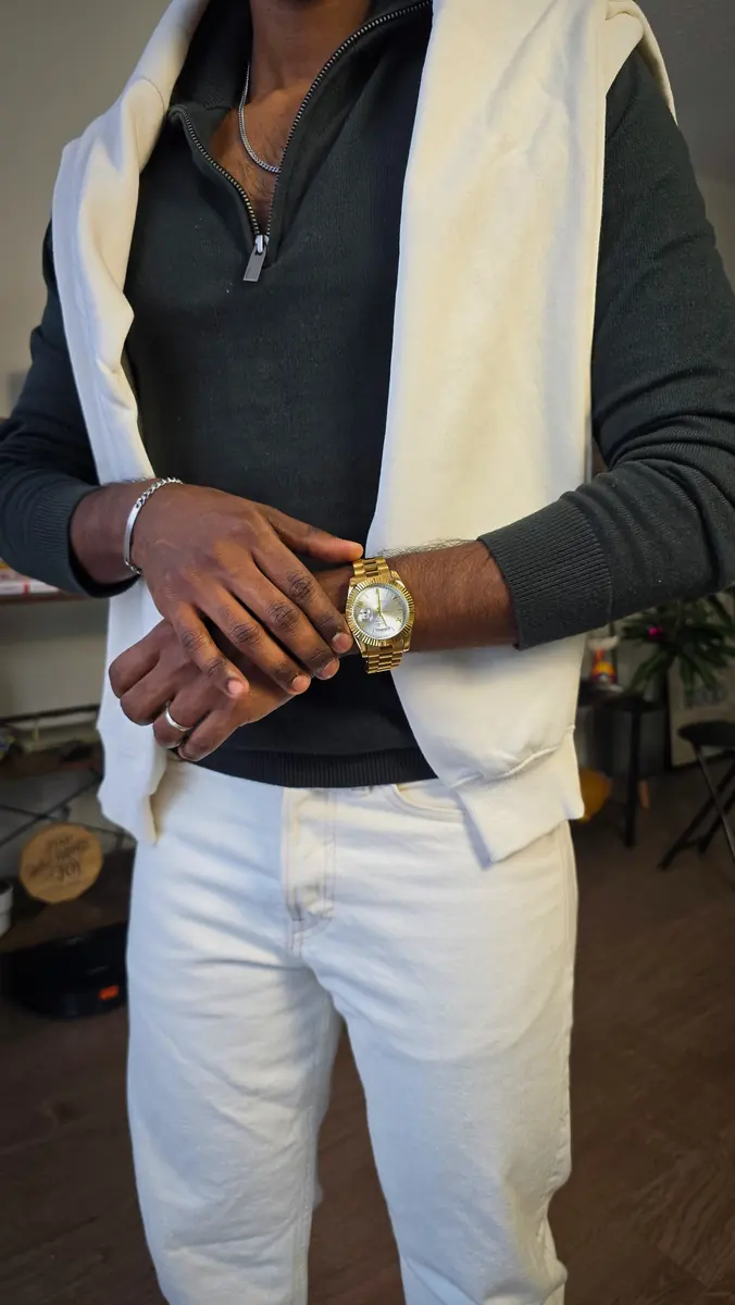 Close-up of a dark quarter-zip layered under a cream hoodie, adjusting a gold watch